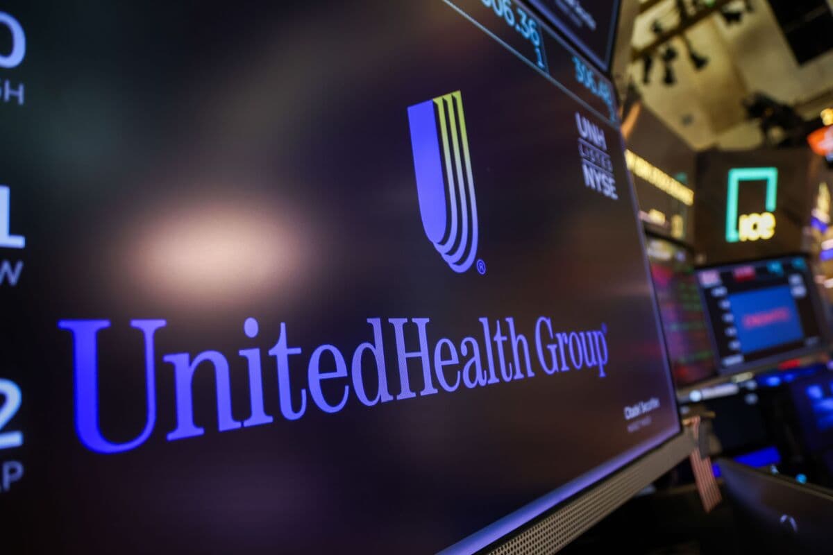 UnitedHealth executives in a boardroom reviewing a large AI dashboard showing automated call metrics and medical…