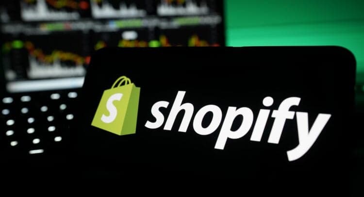 Financial analyst pointing at a rising stock chart on a screen, with Shopify logo visible in background