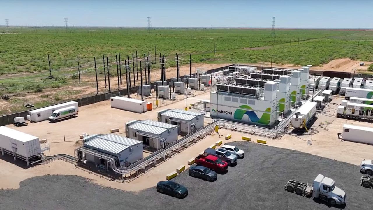 Large industrial gas turbines at a data center site, with warning signs and exhaust stacks, surrounded by chain-link…