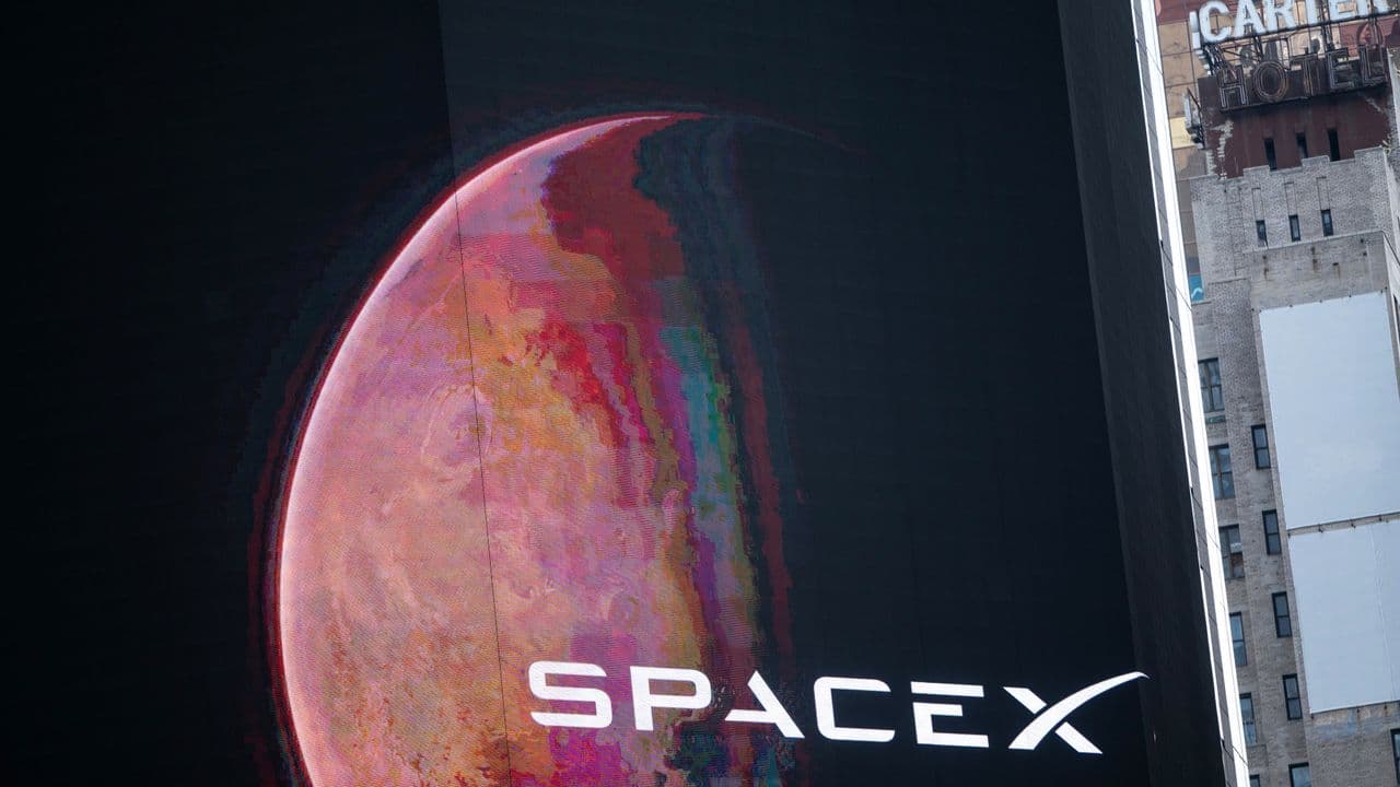 Elon Musk speaking on a stage with a massive glowing server rack backdrop, presenting data center growth projections…