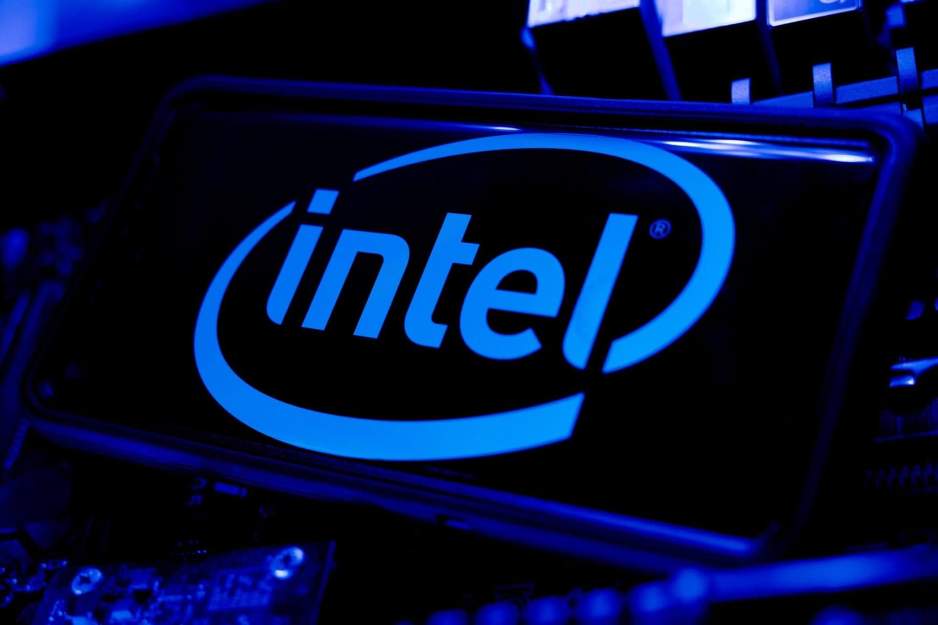 Two executives from Intel and Google shake hands at a press event, with a large screen behind them displaying cloud…
