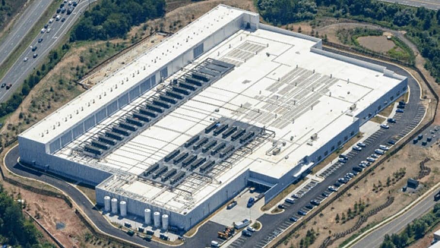 A modern data center building in Manassas, Virginia, with cooling towers and parking lot, representing the $6B joint…