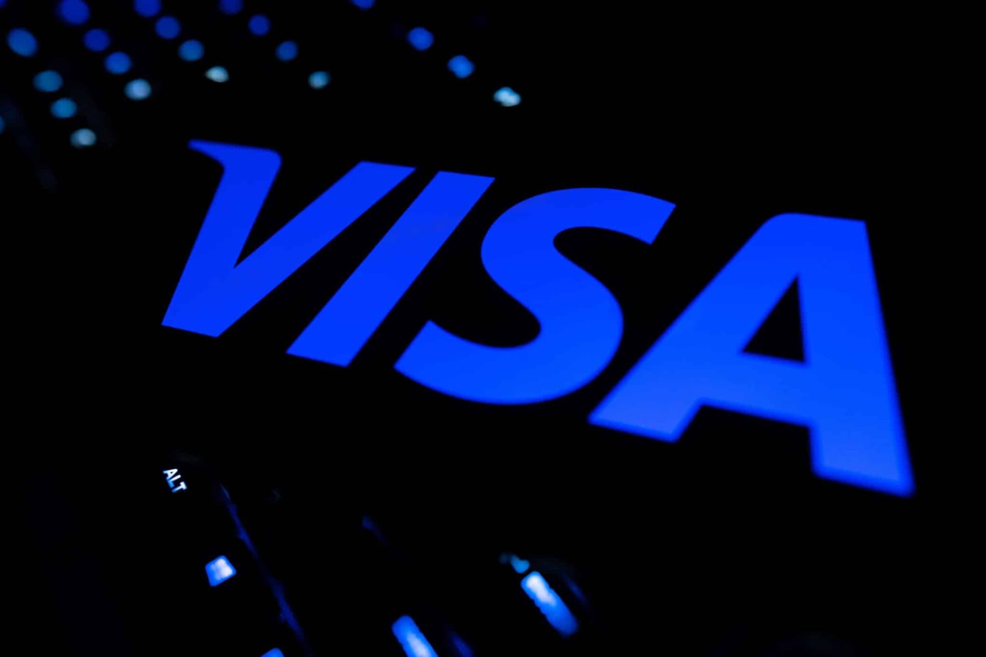 Visa logo on a payment terminal screen, with a person tapping a smartphone to complete a transaction, symbolizing…