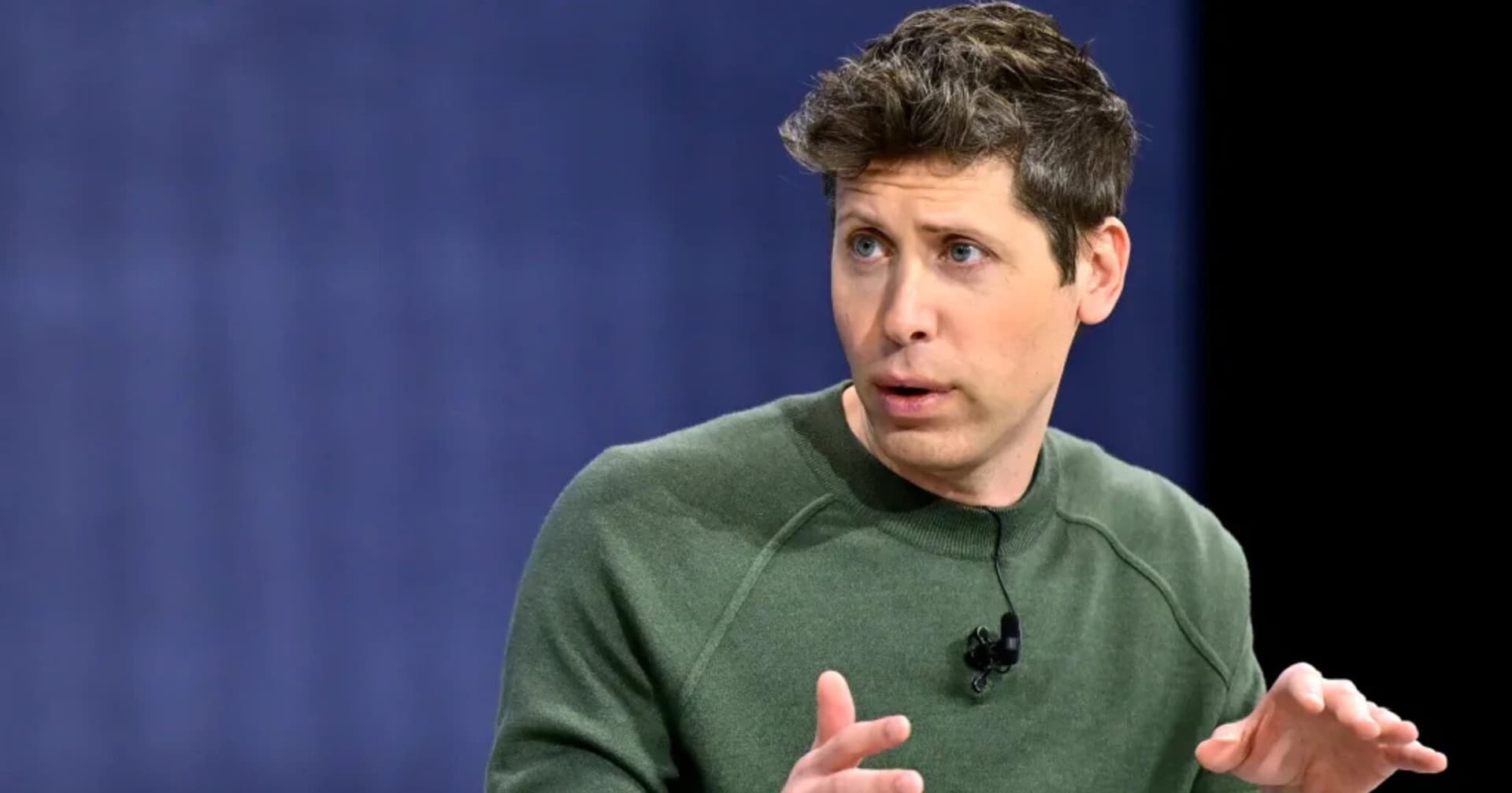 Sam Altman speaking at a tech event, gesturing while discussing AI's impact on coding productivity