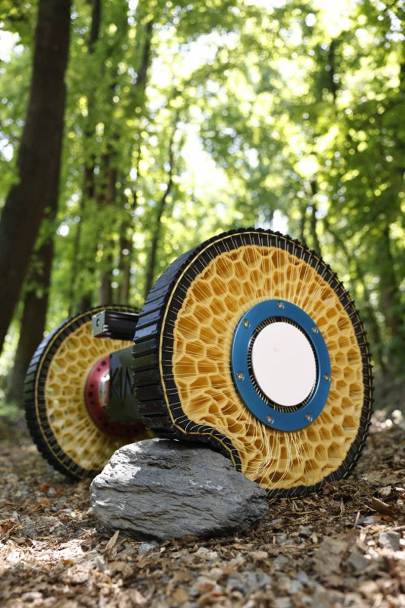 A close-up of a robotic wheel with segmented metal treads and a dark tire, positioned on a textured surface…