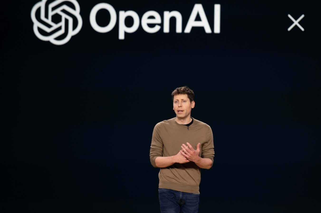 Jakub Pachocki speaking at a podium, with a projected AI data visualization behind him, addressing an audience in a…