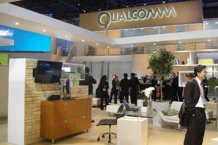 Qualcomm executive holds a processor chip against a blurred background of server racks, highlighting the company's…