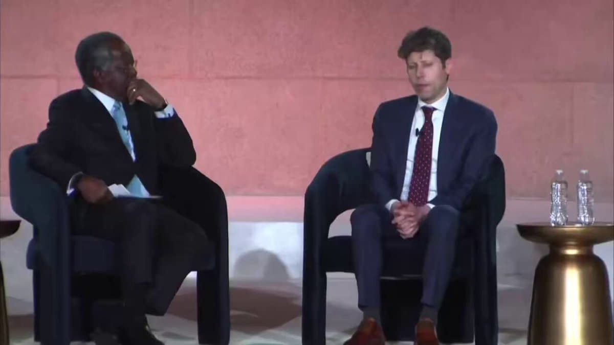 Sam Altman speaks on stage, gesturing with one hand, with a slide behind him showing a graph and the phrase 'AI as a…