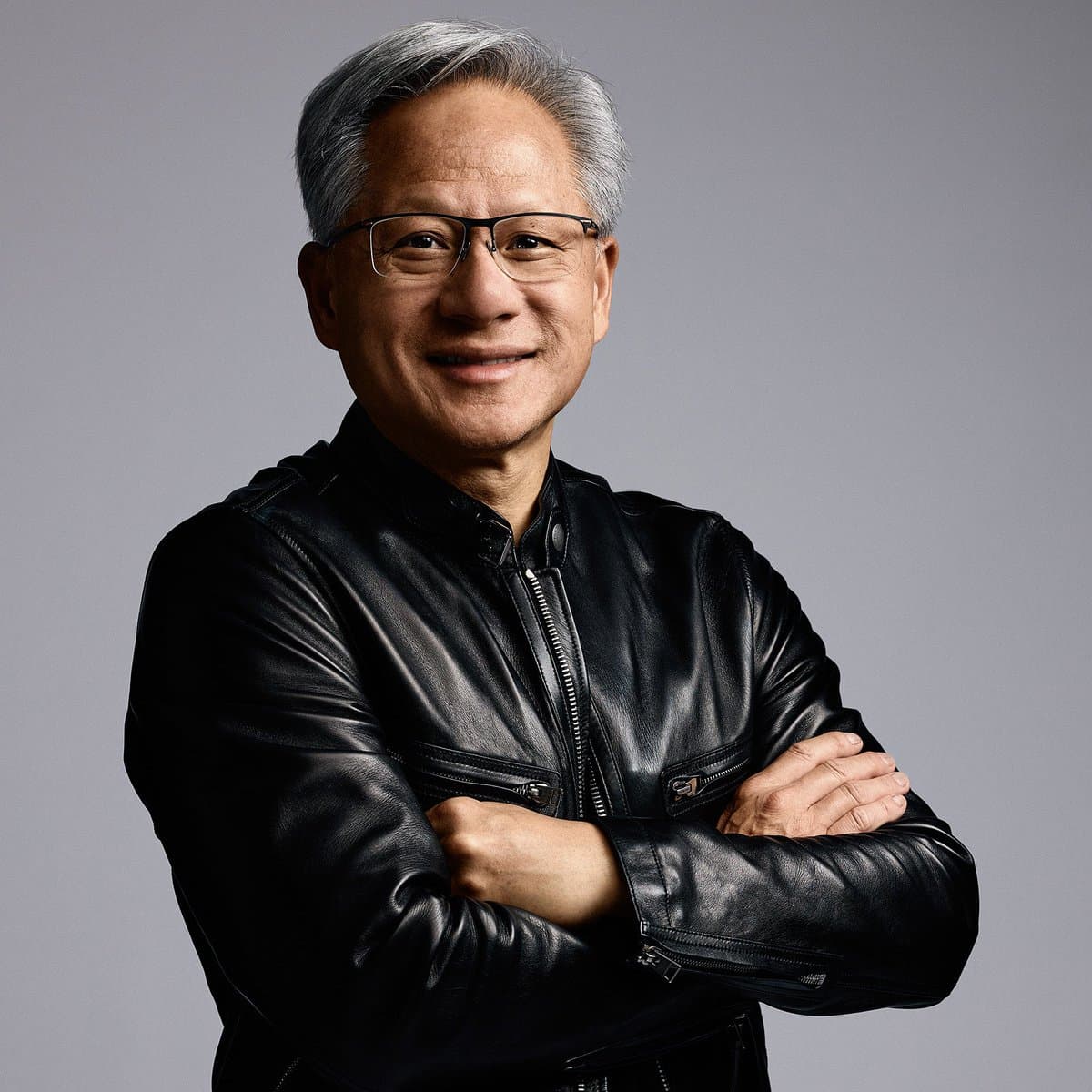 Jensen Huang wearing a black leather Tom Ford jacket, smiling while speaking at an event with a microphone and…