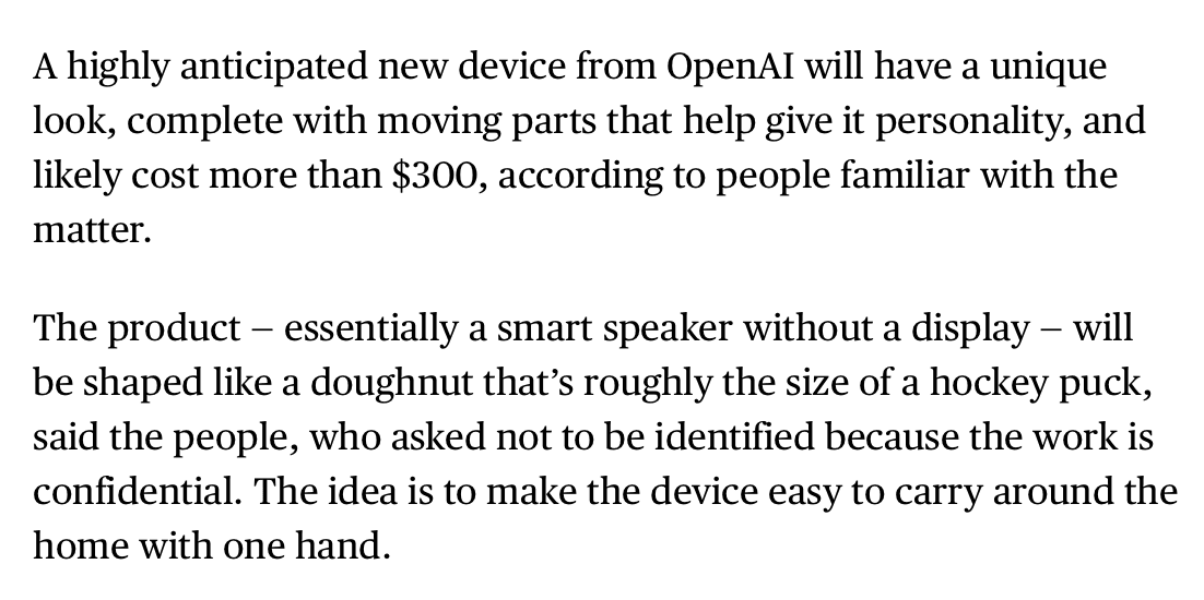 A round, doughnut-shaped smart speaker with a fabric finish sits on a wooden table, held by one hand, no screen…
