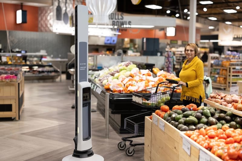 Autonomous shelf-scanning robot navigates a grocery aisle, using cameras to monitor inventory while a shopper…
