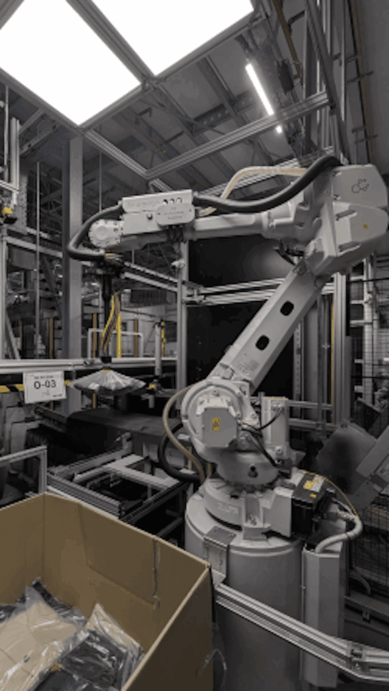 Orange robotic arms in a Zalando warehouse sorting folded clothes on a conveyor belt, with workers nearby monitoring…
