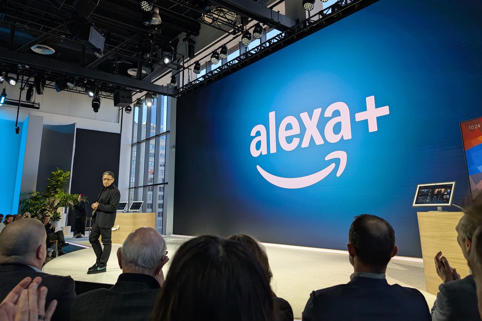 A person tapping a smartphone screen displaying an Amazon shopping cart icon with a glowing AI symbol, surrounded by…