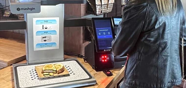 Soccer fan holding a concession item at a self-checkout kiosk with a screen showing items detected by AI computer…