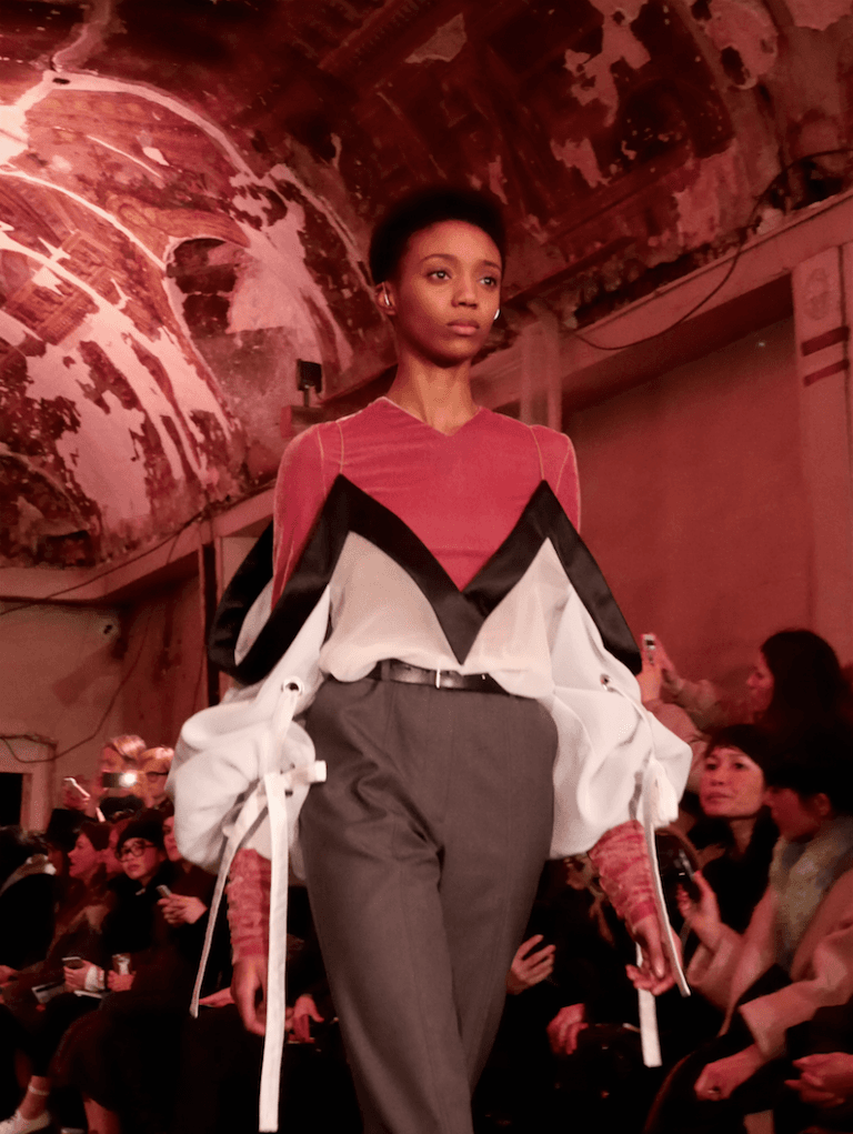 Three young fashion designers in an airy Paris showroom, examining garments on racks and discussing a shared collection