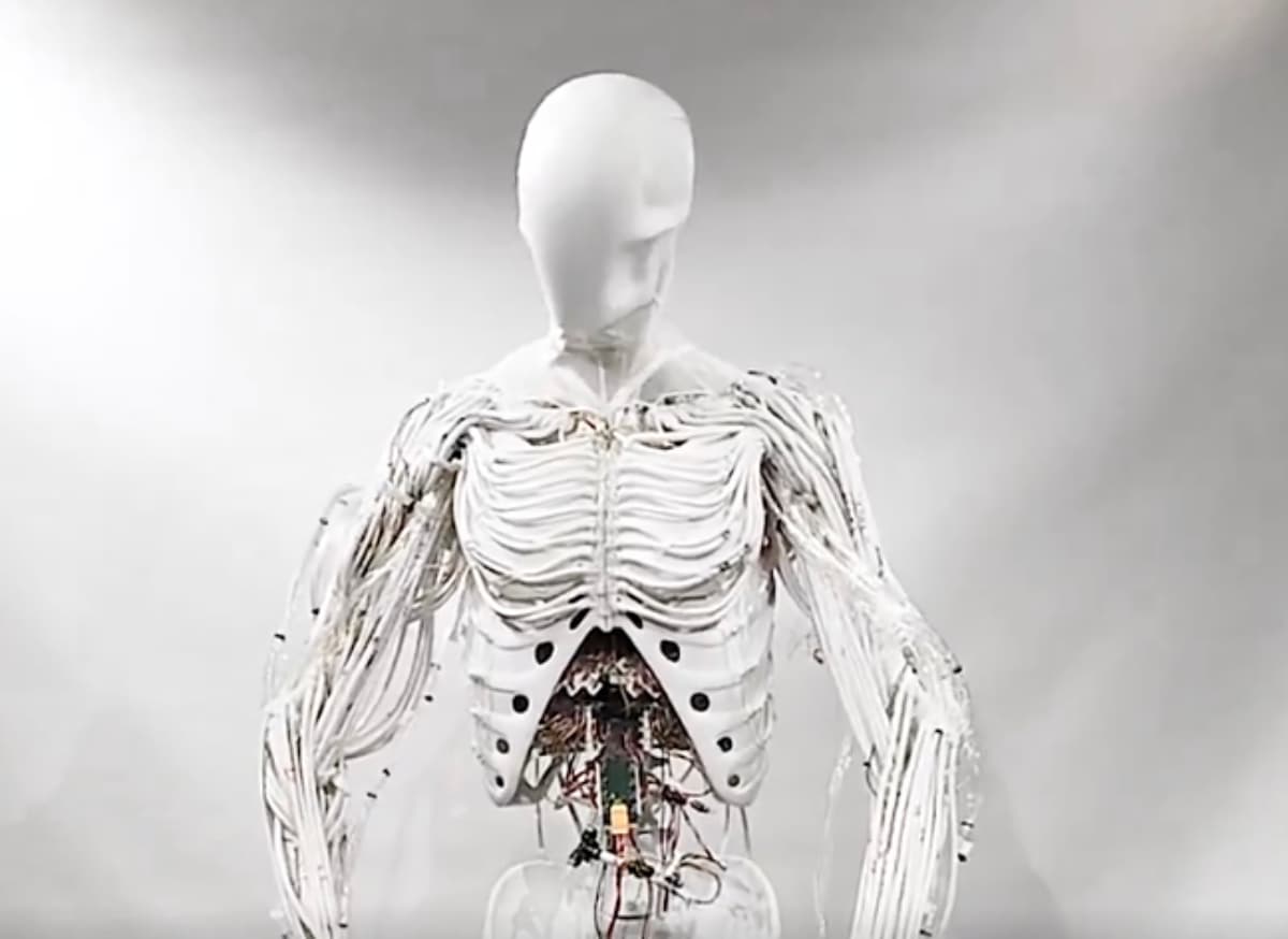 CEO Dhanush Radhakrishnan gestures beside a fluid-actuated humanoid robot with visible artificial muscles…