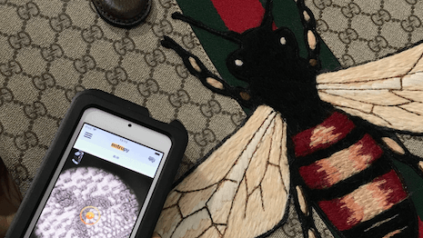 Entrupy handheld scanner analyzing a diamond ring as a jeweler examines it, highlighting AI authentication for…