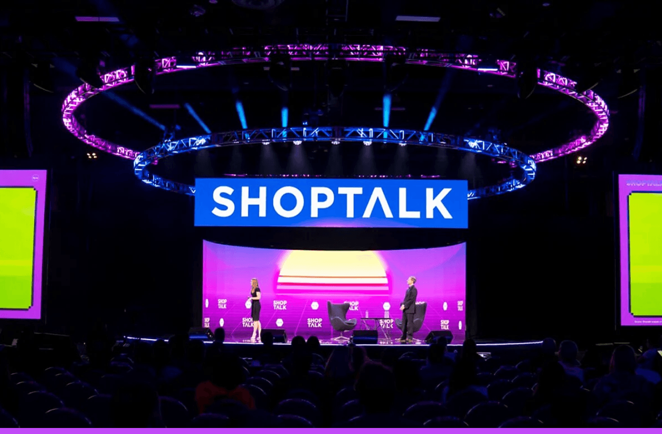 Conference attendees examine a futuristic retail display with AI analytics on a large screen, surrounded by product…