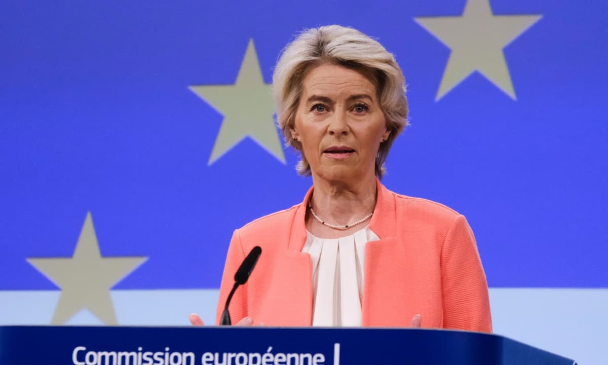 European Commission President Ursula von der Leyen speaks at an AI summit podium, with EU flags behind her…