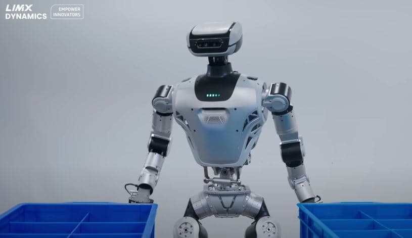 Humanoid robot with 31 joints steps out of a large cardboard shipping box, cables and packing foam visible inside…