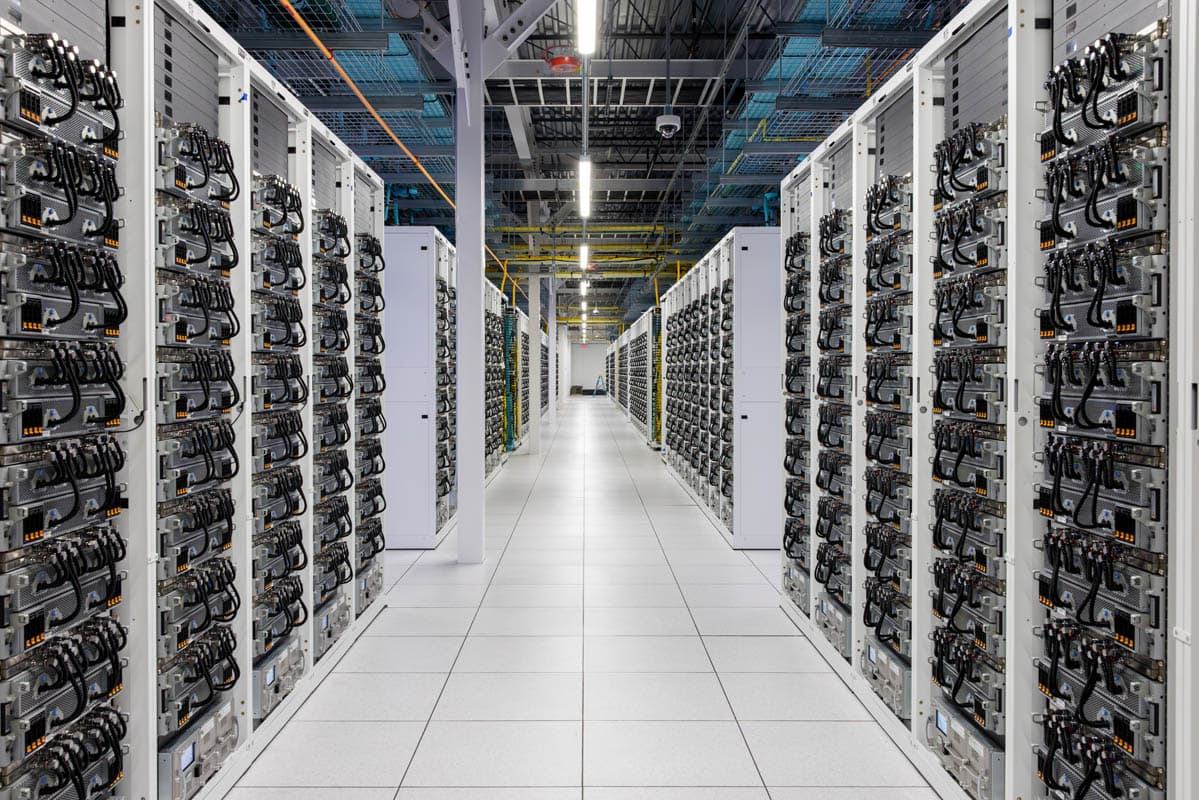 Rows of GPU servers in a brightly lit data center hall with blue LED accents, likely the xAI Colossus cluster in Memphis