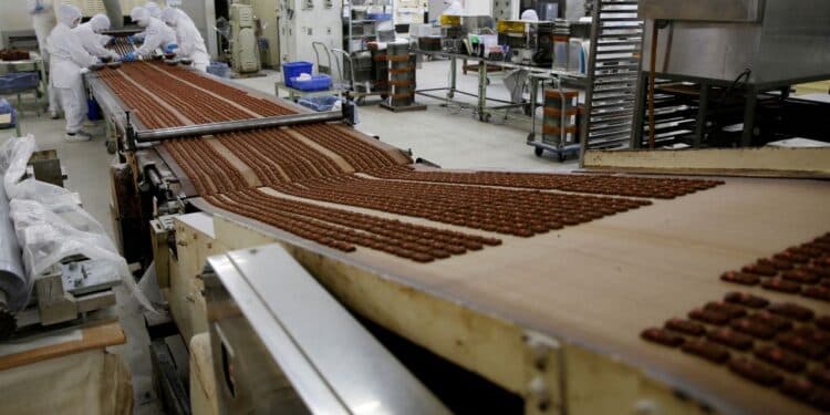 Japanese factory workers collaborate with robotic arms assembling electronics, while an elderly engineer monitors a…
