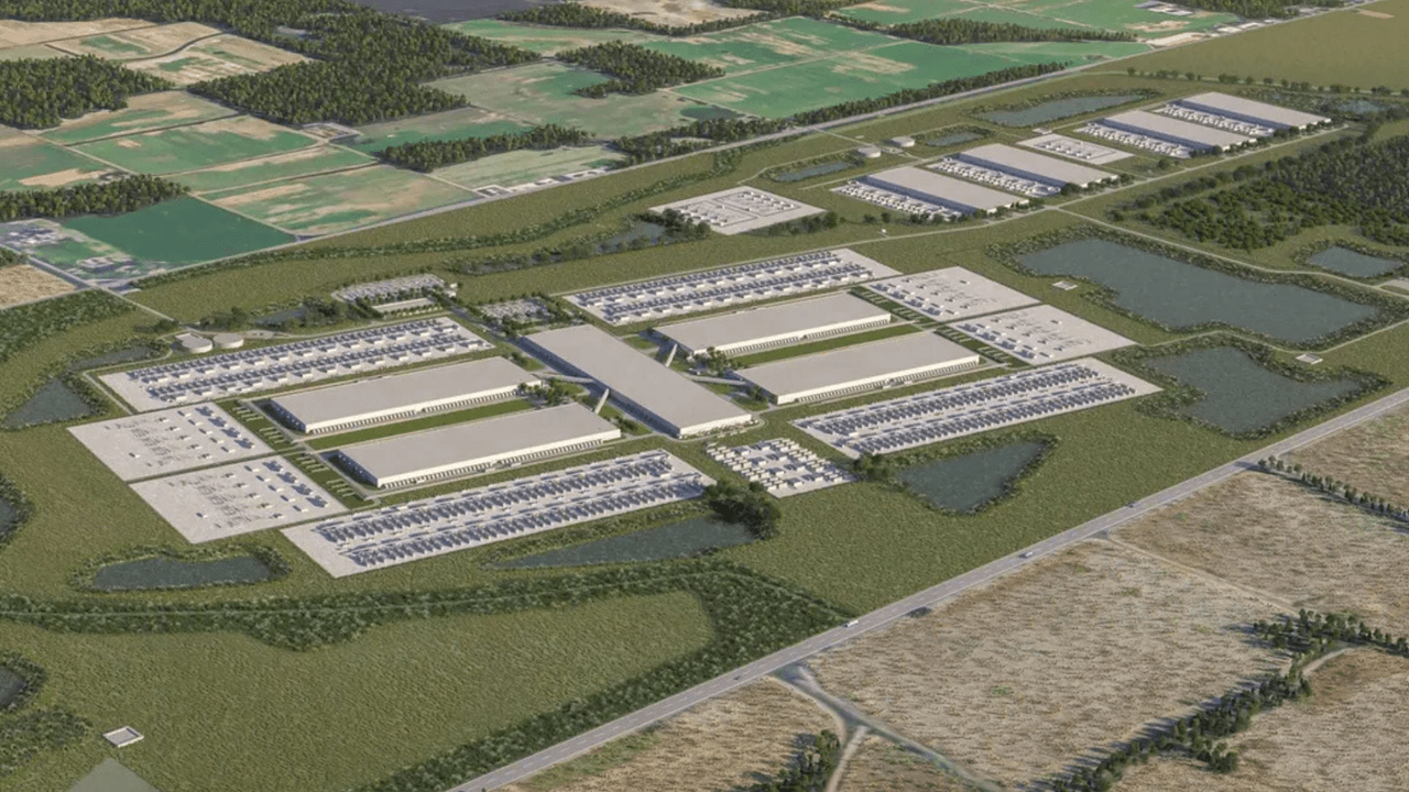 Aerial view of a rural data center complex with rows of white buildings, power lines, and construction equipment…