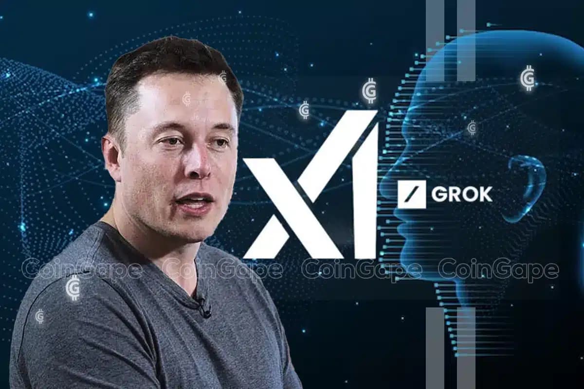 Elon Musk in a dark suit presenting at a tech conference, with a large screen behind him displaying the Grok AI logo…