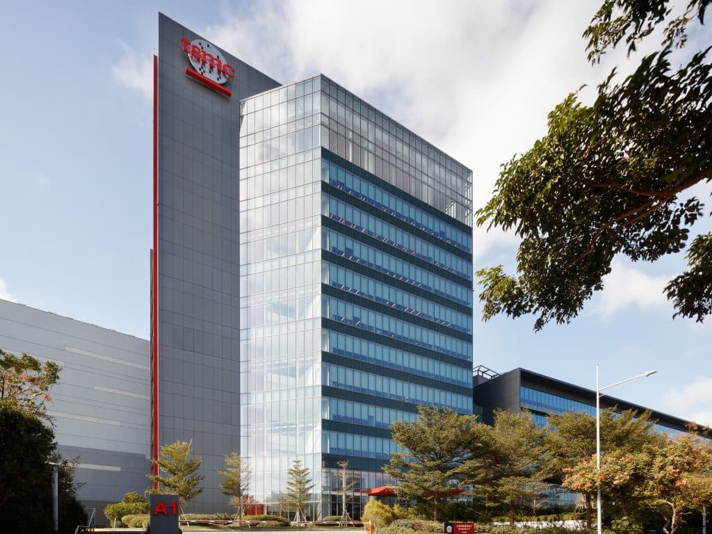 TSMC Fab 15A exterior building, likely in Taiwan, with semiconductor manufacturing equipment visible; the scene…