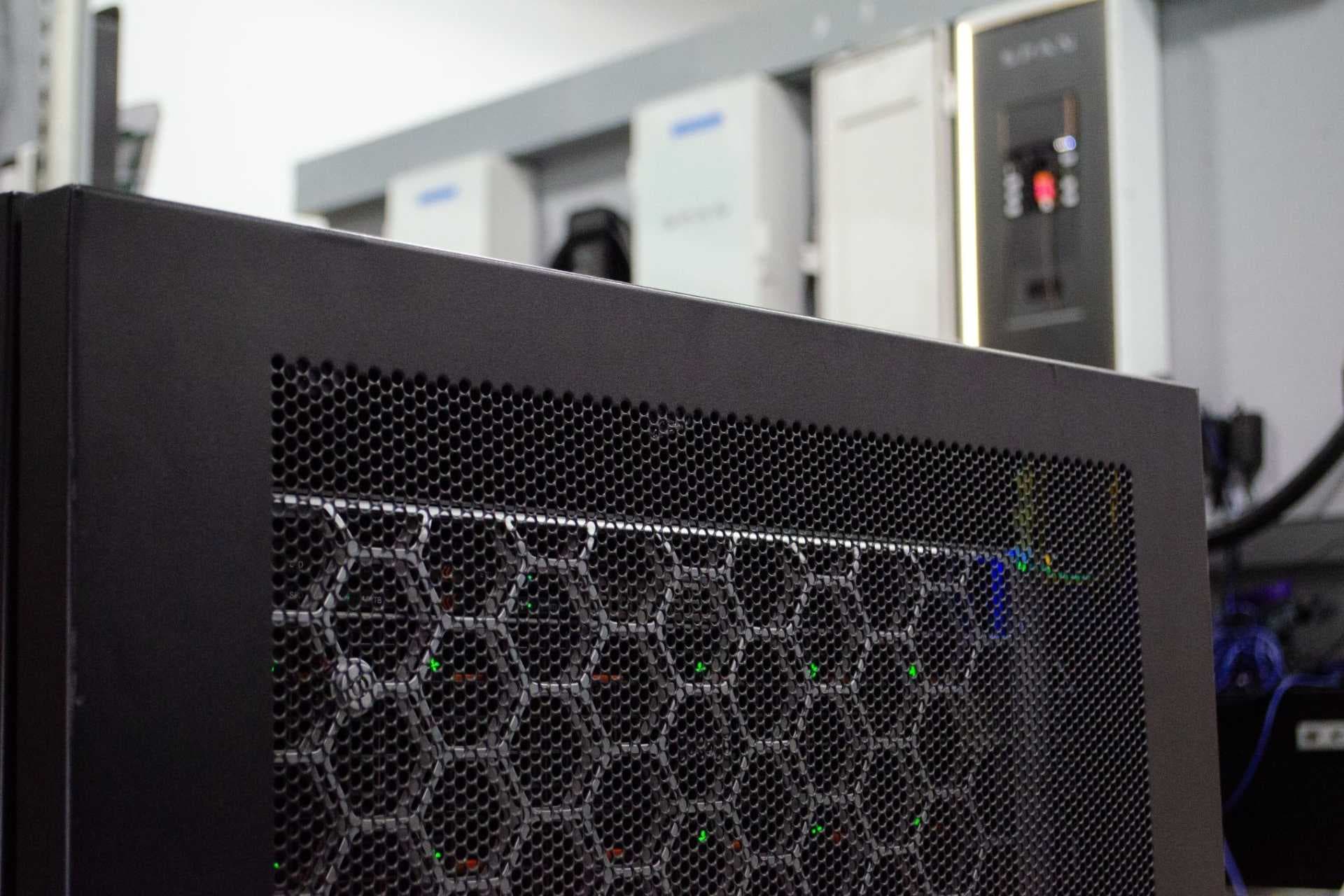 A sleek, compact data center unit mounted on a residential basement wall, with glowing blue status lights and cables…