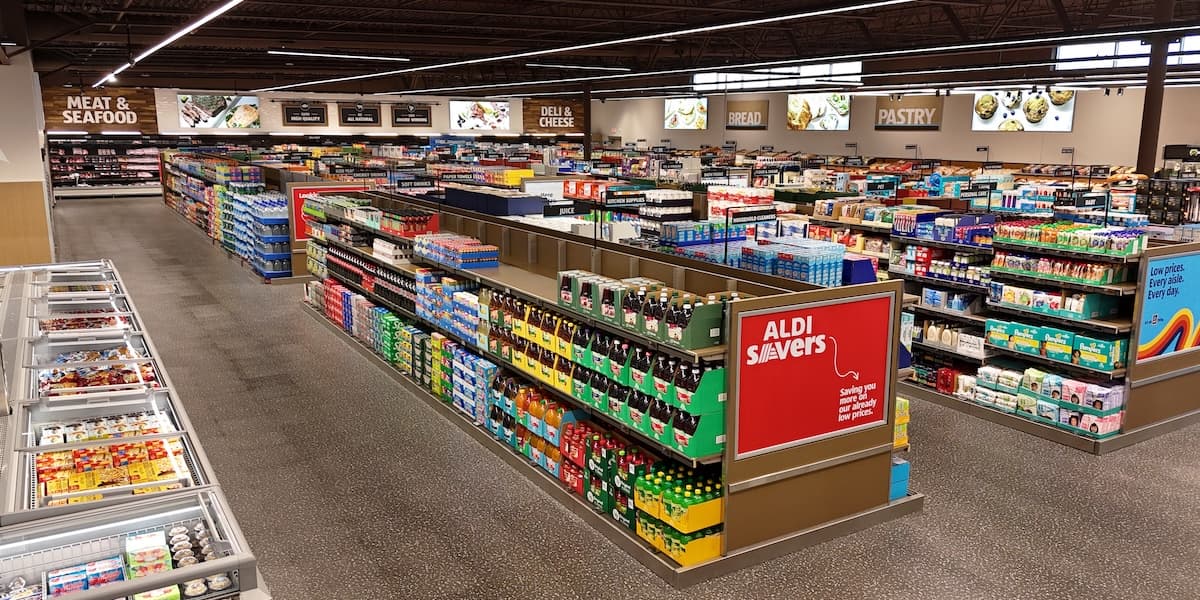 Shoppers browse aisles in a bright Aldi grocery store with neatly stacked shelves and produce displays