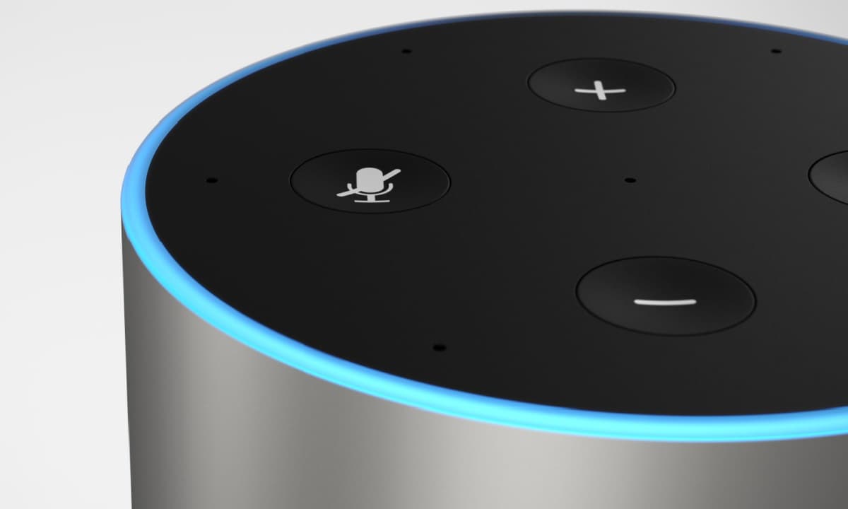 A person speaks to an Amazon Echo smart speaker on a kitchen counter, while a smartphone screen displays a product…