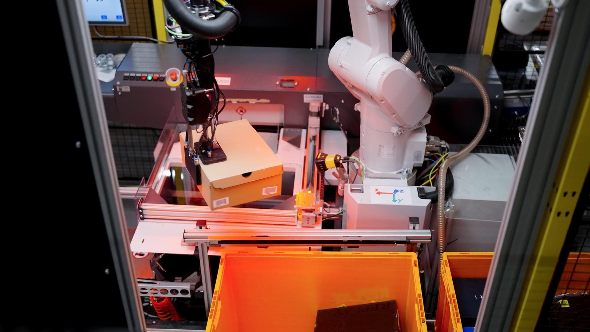 Robotic arms in a warehouse sort packages on a conveyor belt, with workers nearby in a brightly lit logistics center
