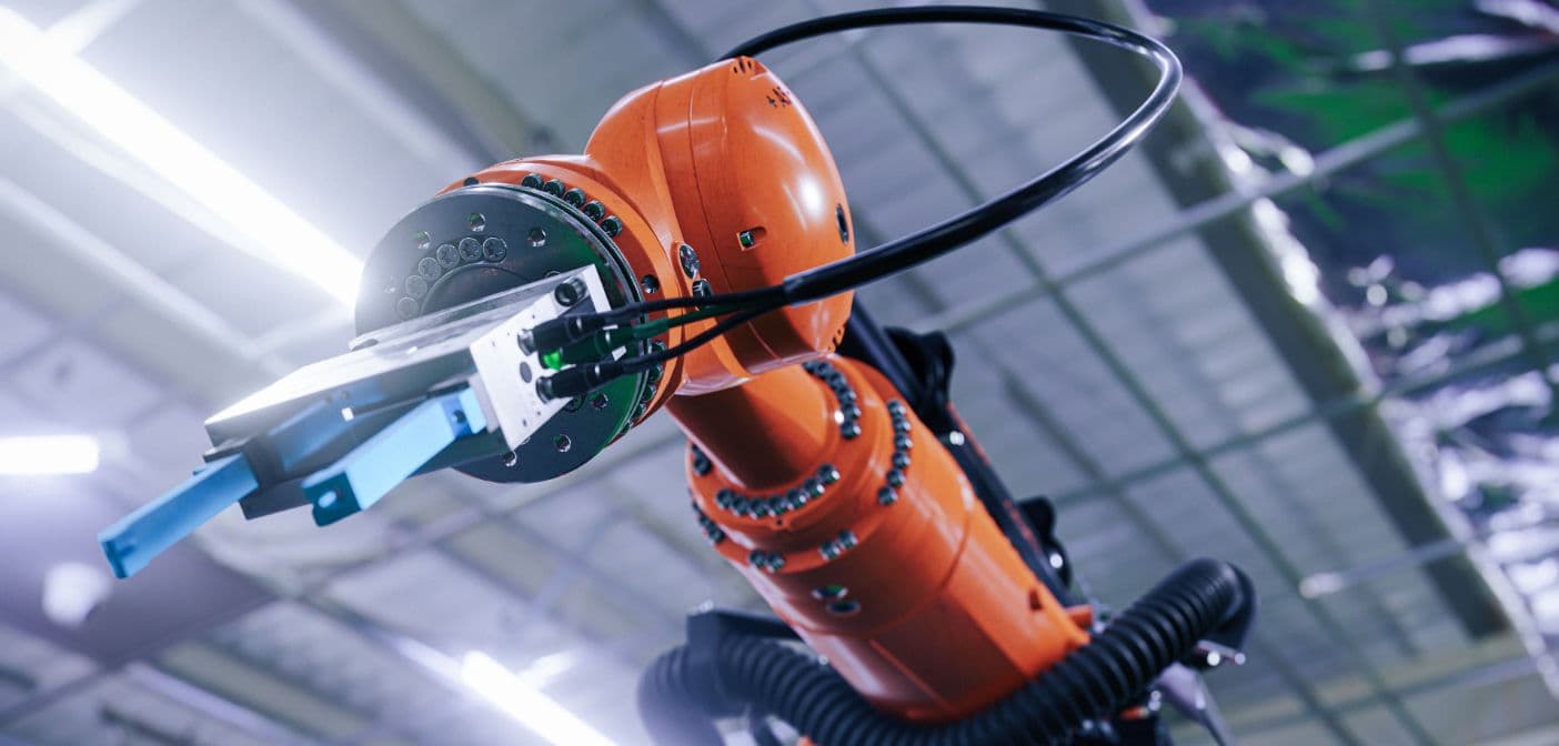 A person wearing a motion-tracking glove controls a giant metal robotic hand that mimics their movements in a workshop