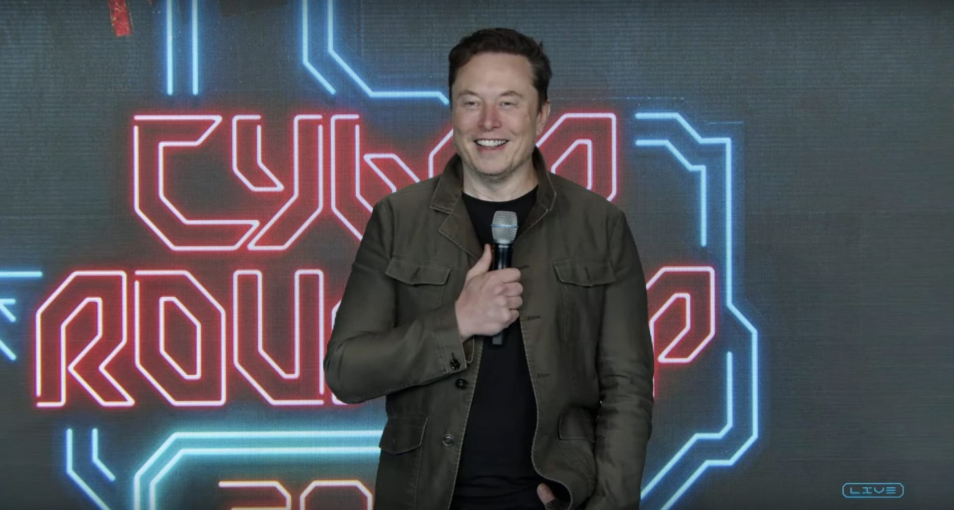 Elon Musk stands at a podium on stage during Tesla's annual shareholder meeting, speaking to an audience in a large…